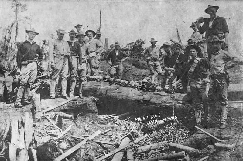 Black and white photo of American soldiers posing with skulls lined up on a log.