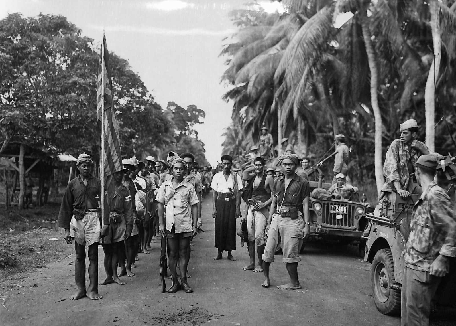 Photo of Filipino soldiers lined up, holding the American flag jeeps next to them