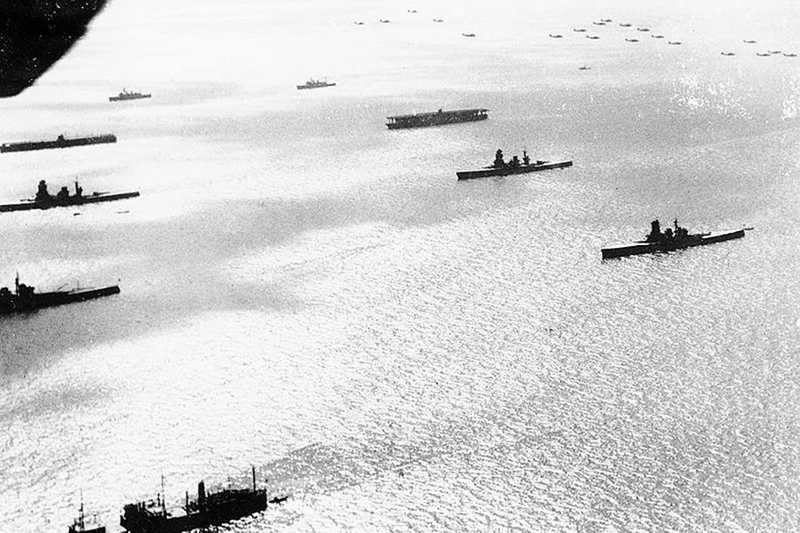 Black and white aerial photo of battleships cruising through the ocean