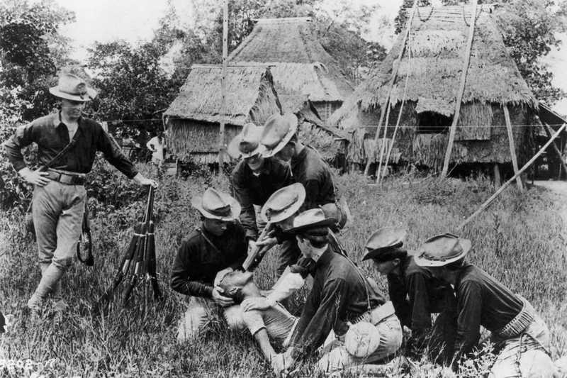 Black and white photo of American soldiers holding down a Filipino and pouring water onto his face